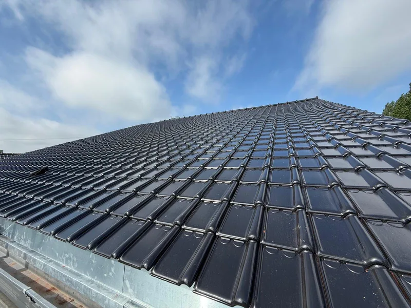 Toiture en tuiles noires vernissées avec corniche en zinc
