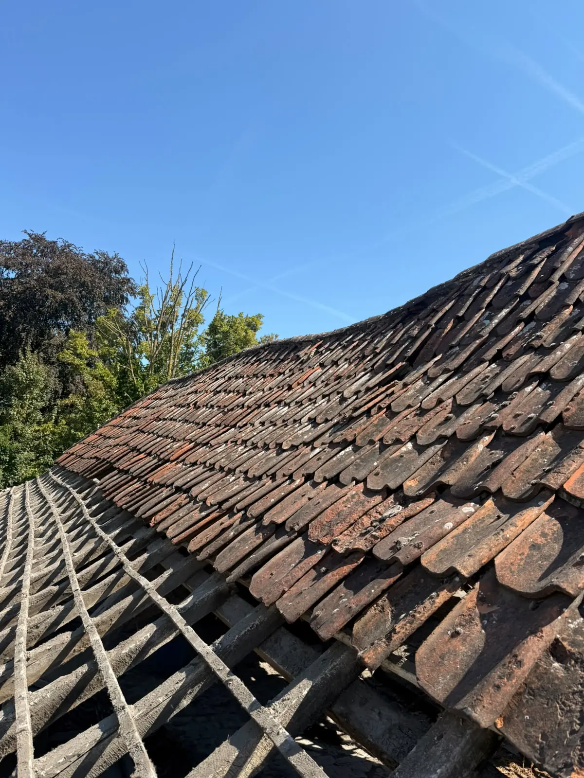 Anciennes tuiles en terre cuite usées et lattage affaissé avant rénovation à Tournai
